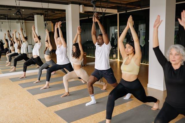 Företagsyoga Stockholm. Personer som står på grå yogamattor i en lokal med höjda armar.