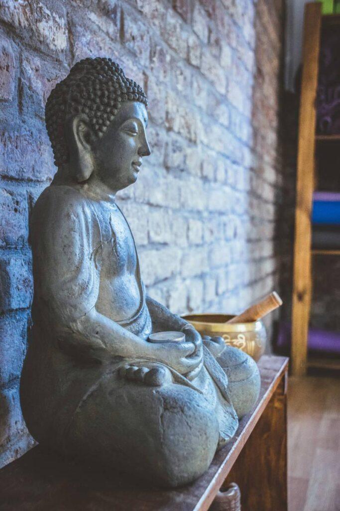 Buddha staty i sten på en träbänk med klangskål bredvid.