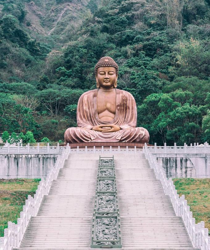 Trappor som leder till en hög Buddha staty med skog bakom.