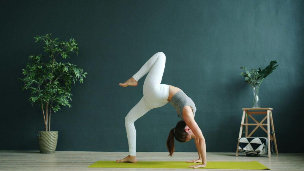 Kvinna gör en backbend på en ljusgrön yogamatta med en turkosvägg bakom henne.